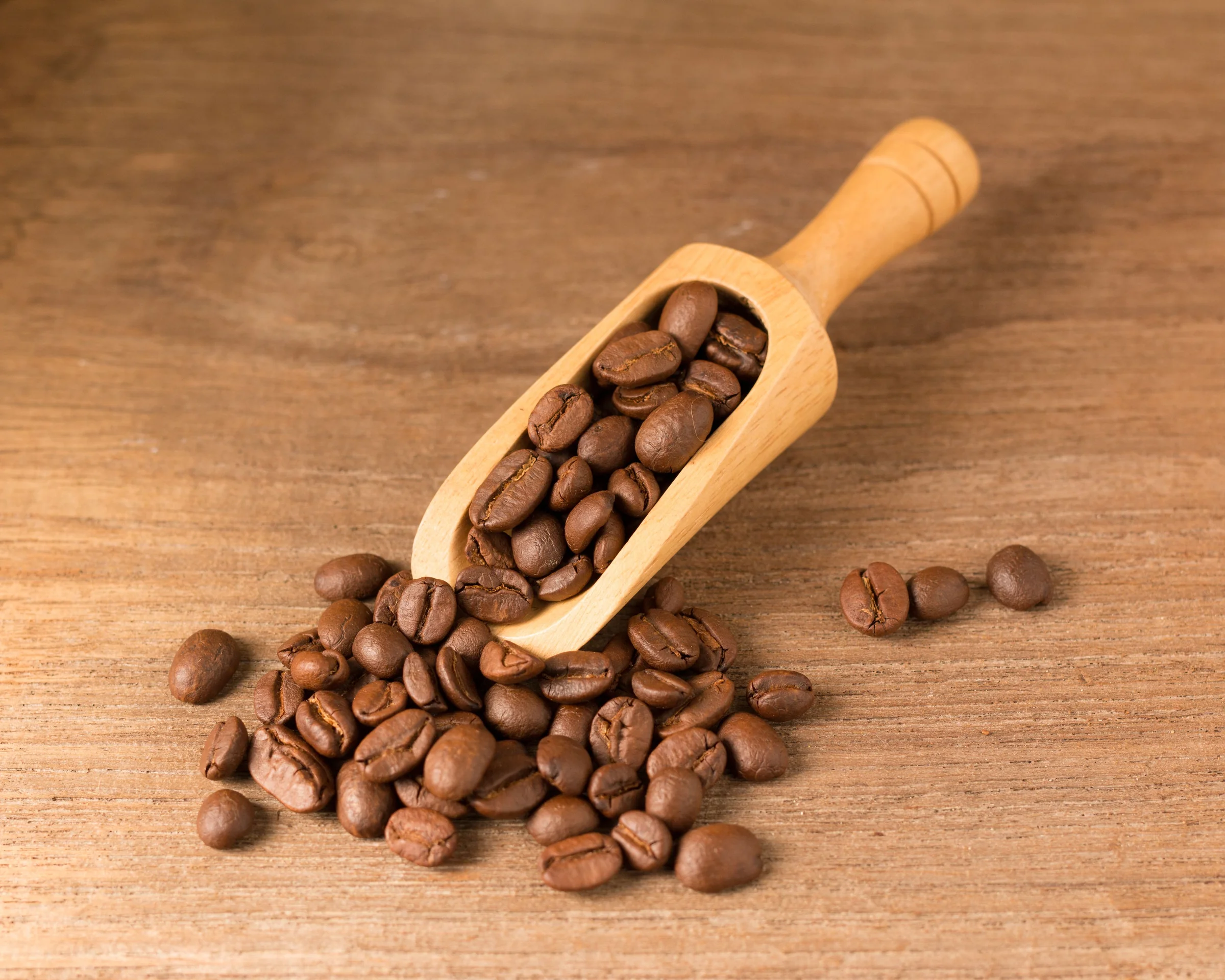 Roasted coffee beans spilling from a wooden scoop