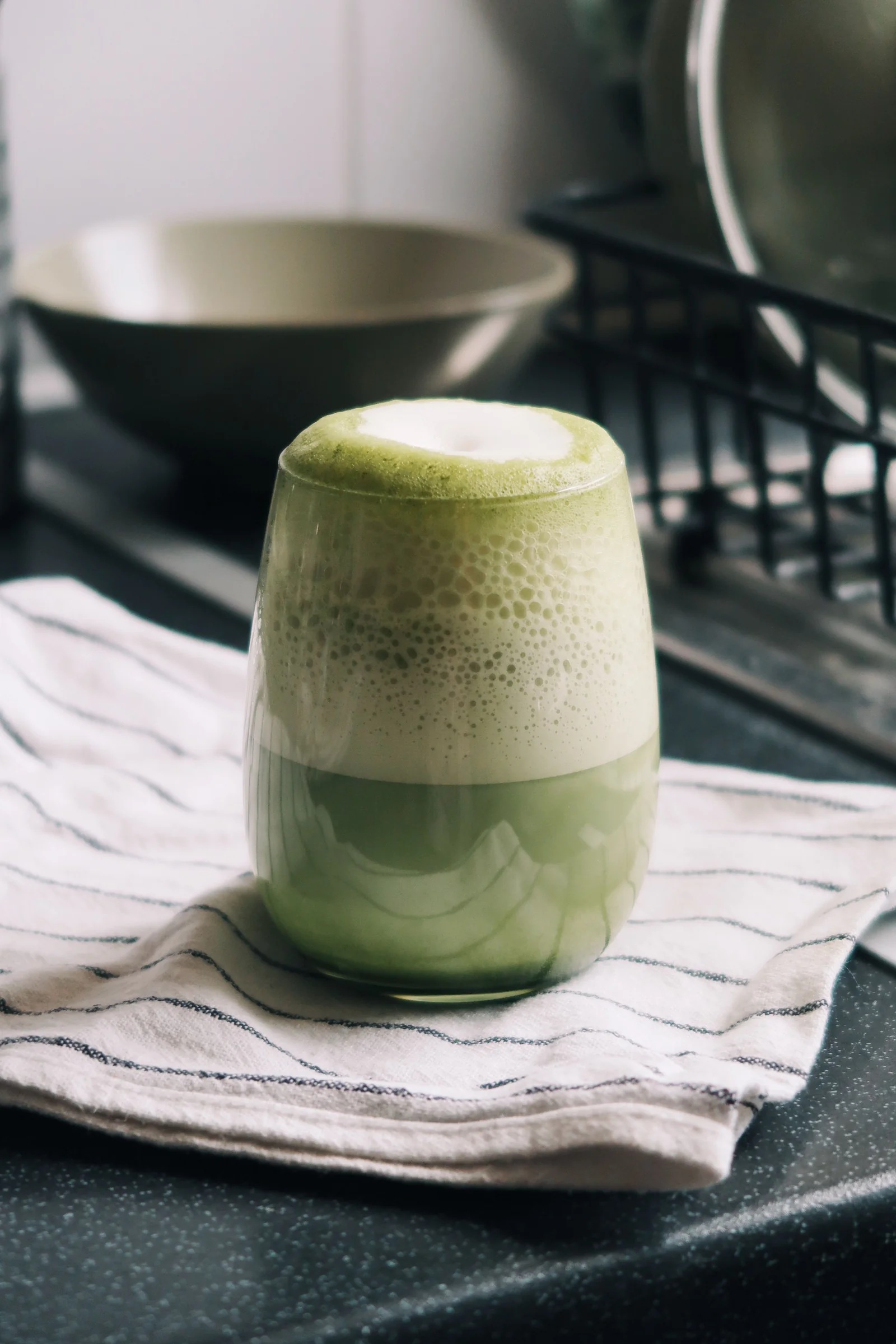 A frothy matcha latte in a glass on a striped towel