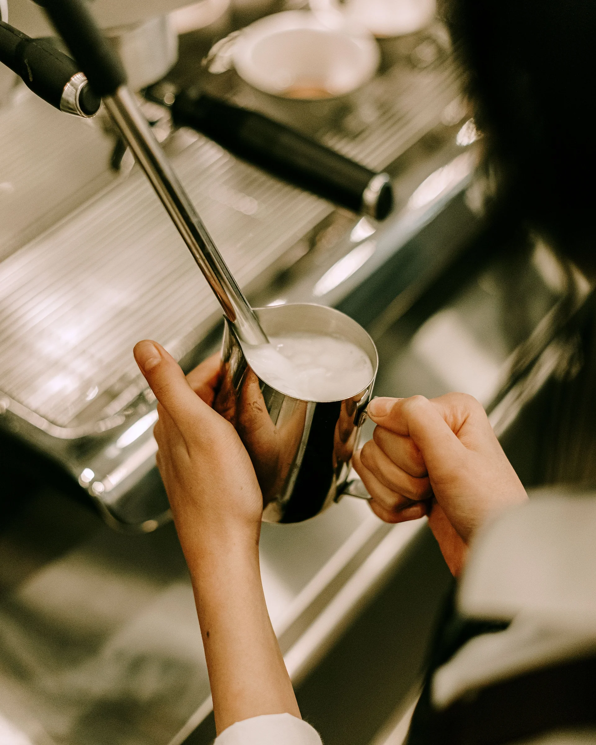 A barista steaming milk in a stainless pitcher at an espresso machine