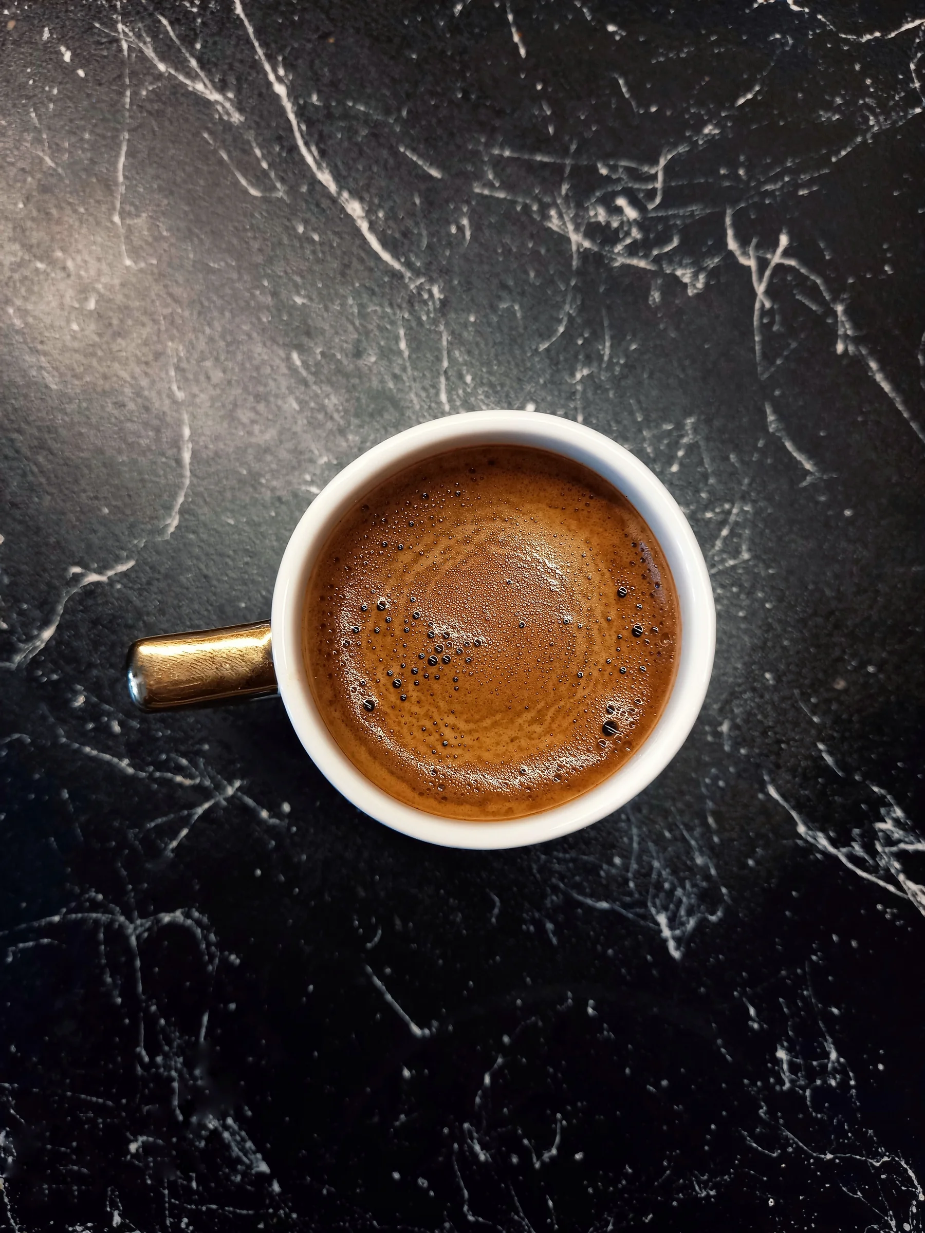 A small cup of espresso with crema on dark marble, from above