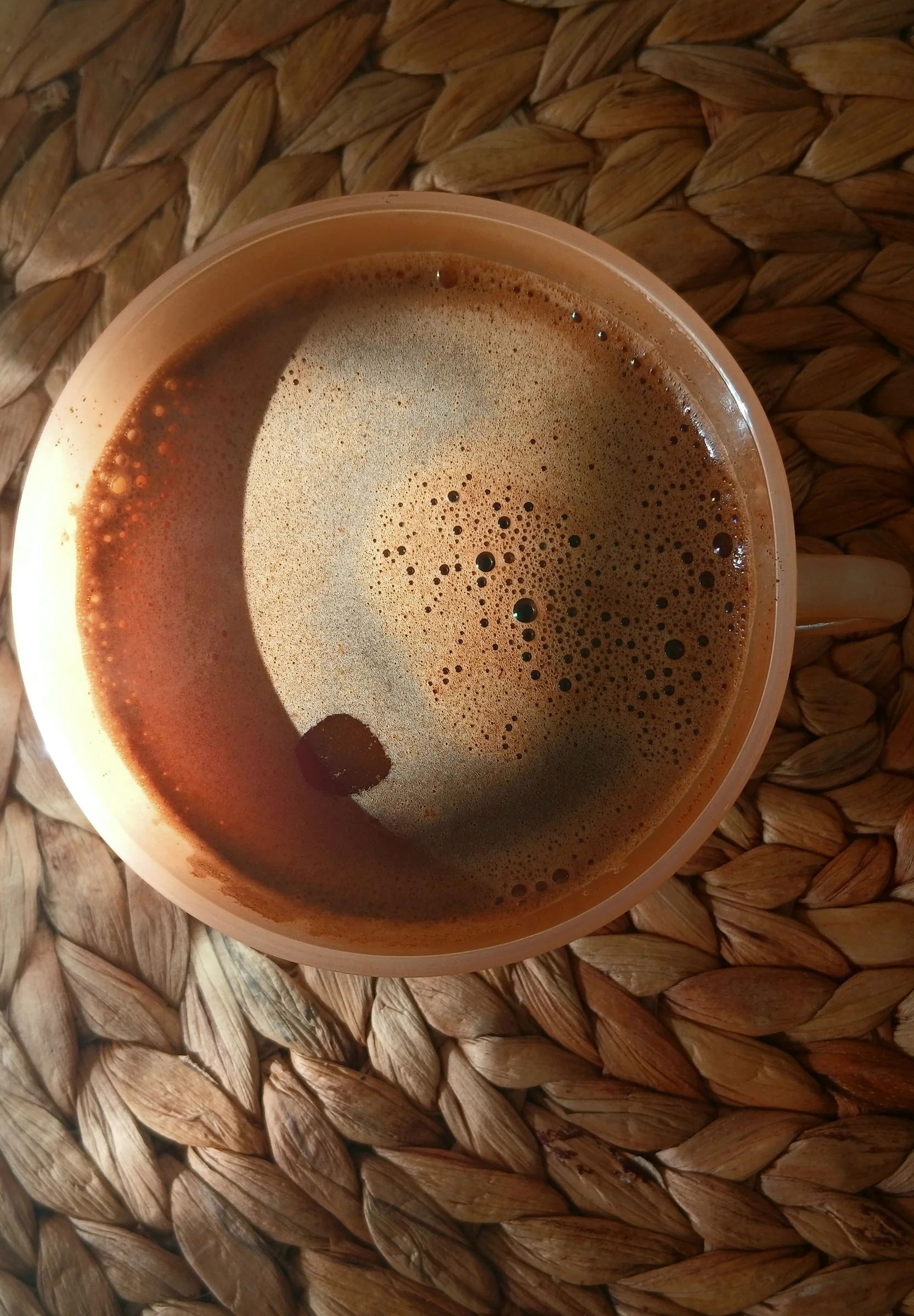 A cup of coffee with foam on a woven mat, from above